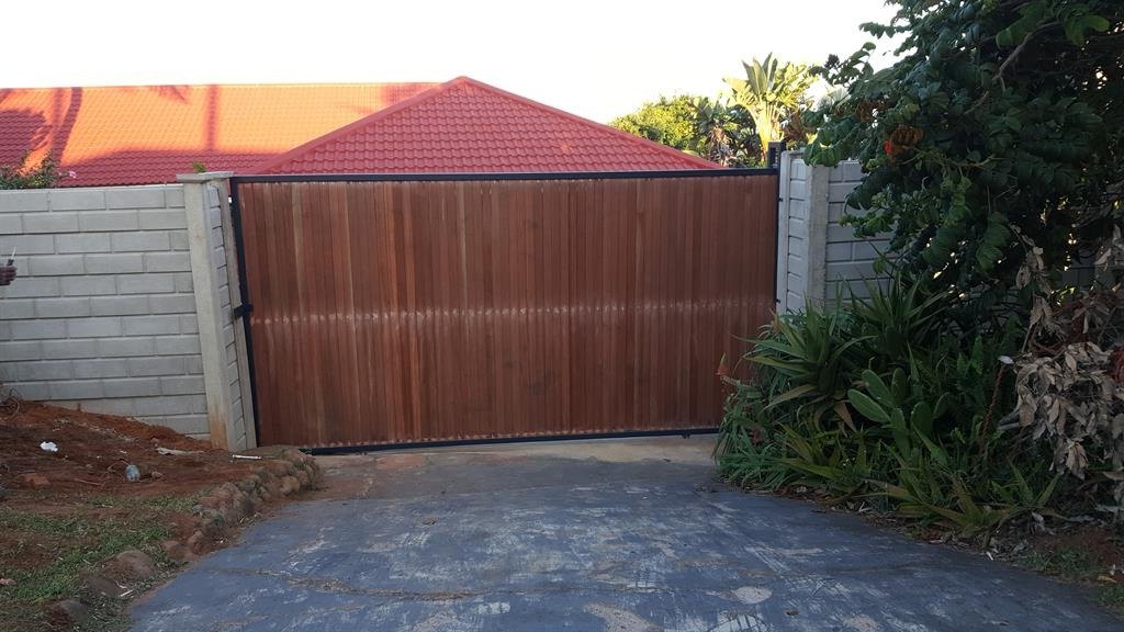 A timber driveway gate set in a brick boundary wall